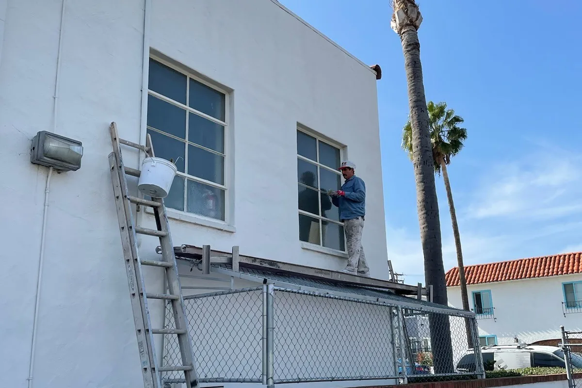 Ladders set along the two-story stucco wall, a Tony's Painting job in San Diego County
