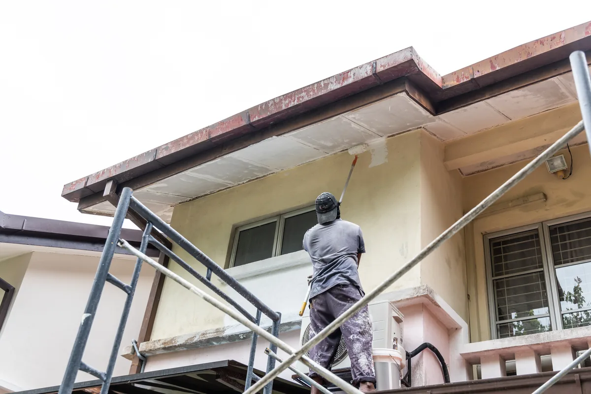 Painter on scaffolding painting the stucco exterior of a two-story home with a tile roof