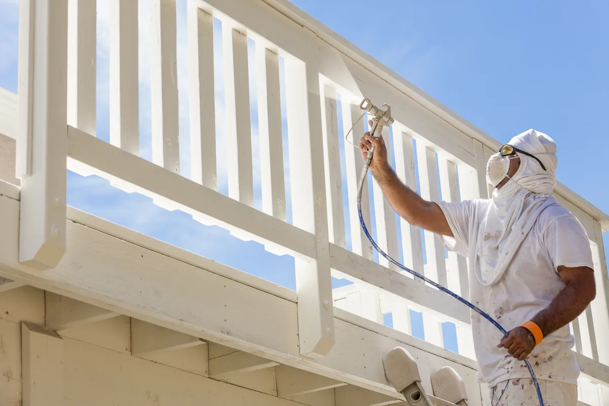 Painter spraying a wood deck railing white