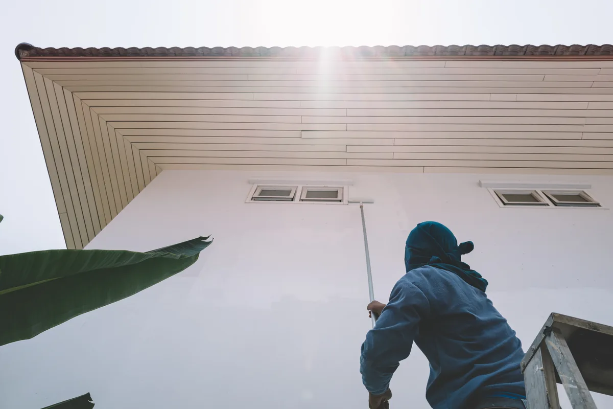 Painter rolling fresh paint under the eave of a stucco home with a tile roof